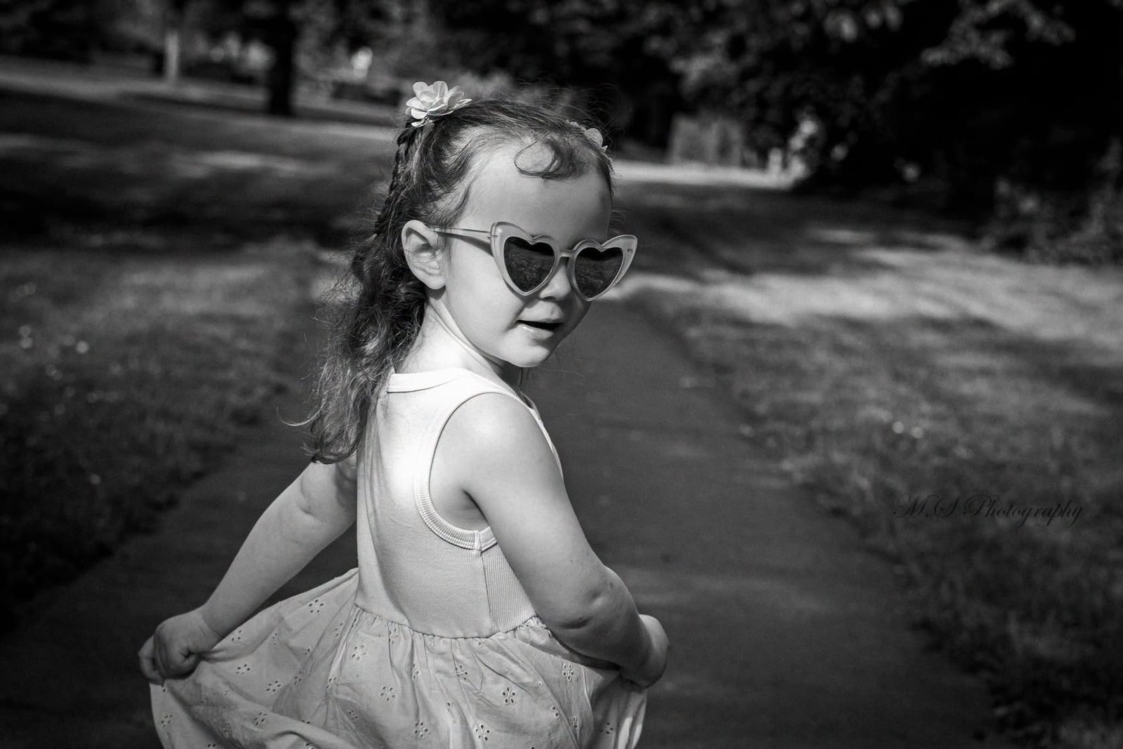 A little girl in heart-shaped sunglasses in the park, in black and white