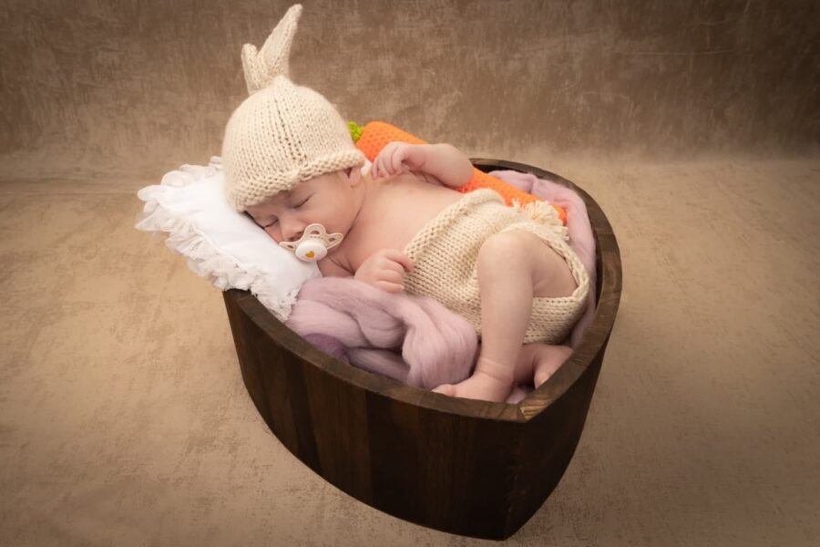 A newborn asleep in a wooden bowl in a knitted bonnet