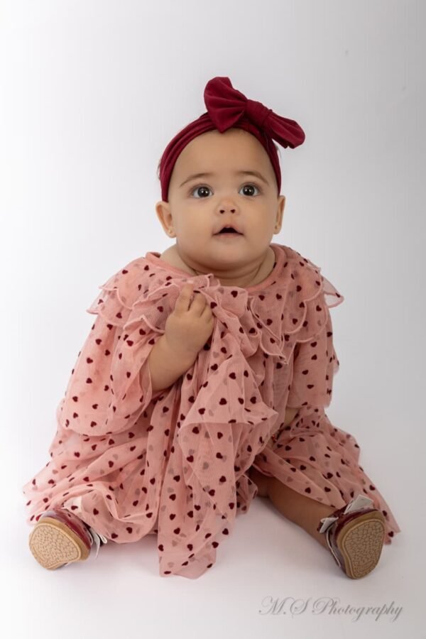 A baby girl in a red headband and polka-dot dress