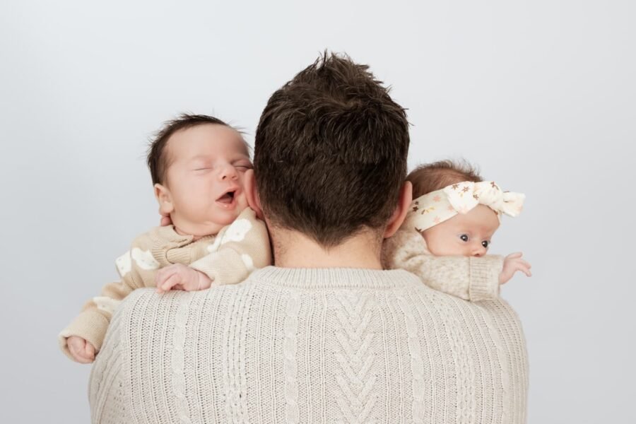 A parent holding two newborns over the shoulder
