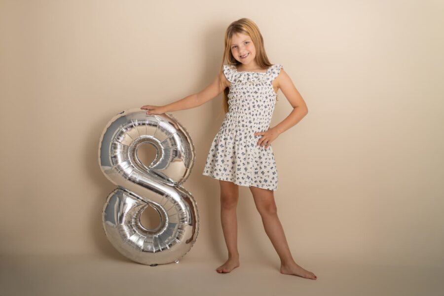 A girl standing beside a silver number-eight balloon in the studio
