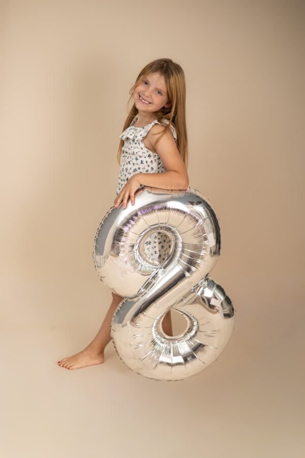 A girl at her eighth-birthday studio session with a silver number-eight balloon